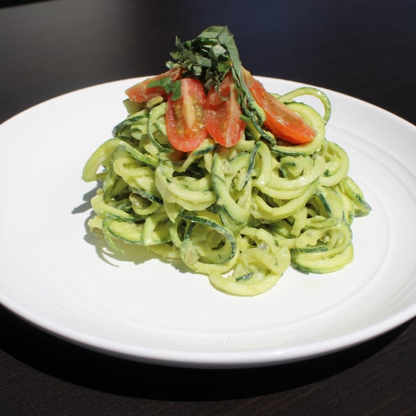 Zucchini noodles with creamy avocado sauce, topped with halved cherry tomatoes and fresh basil.