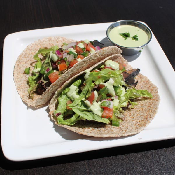 Two healthy tacos with lettuce, salsa, and green sauce, served with a side of green dressing.