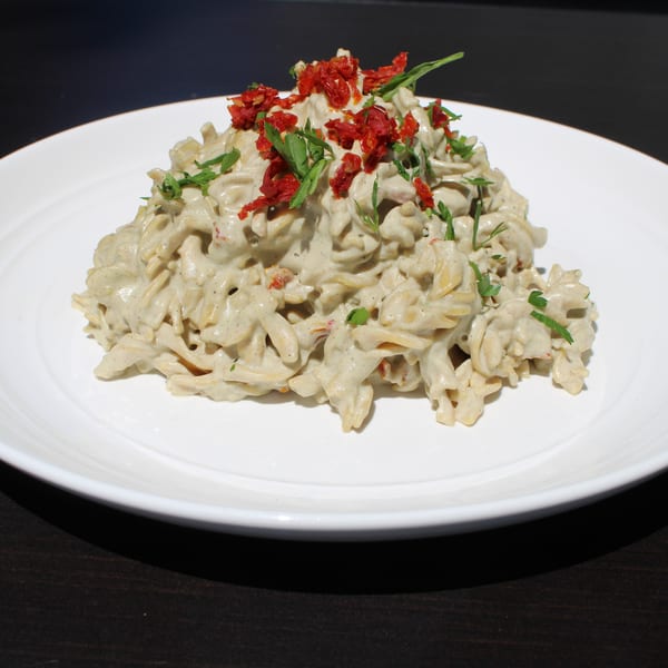 Creamy pasta with sun-dried tomatoes and fresh herbs on a white plate at Garden Kitchen.