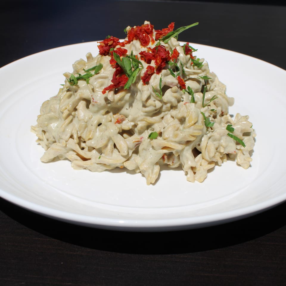 Creamy pasta with sun-dried tomatoes and fresh herbs on a white plate at Garden Kitchen.
